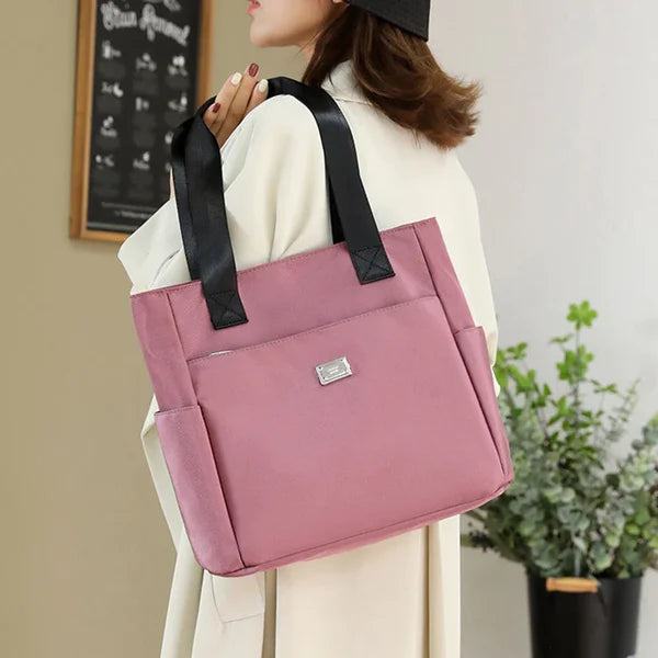 Donna con borsa tote rosa in tessuto, manici neri, indossa cappotto beige. Accessorio moda elegante, ideale per shopping e uso quotidiano.