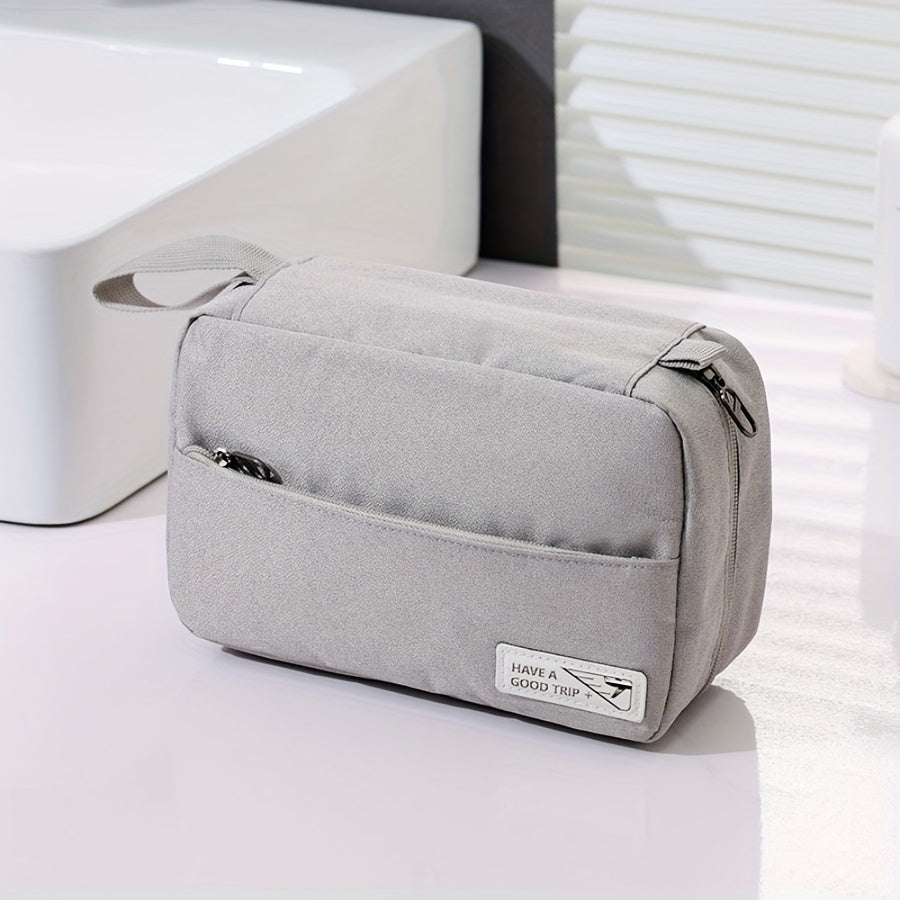 Borsa da toilette grigia con cerniere, tasca frontale e manico, su un piano del bagno. Ideale per viaggi, organizzazione accessori bagno.