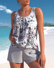 Donna in spiaggia con top floreale bianco e nero, dettagli leopardati, e pantaloncini grigi. Moda estiva, abbigliamento casual mare.