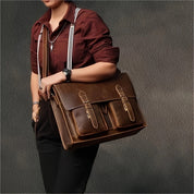 Borsa a tracolla in pelle marrone, design vintage, con fibbie e tasche frontali, indossata da persona con camicia bordeaux e pantaloni neri.
