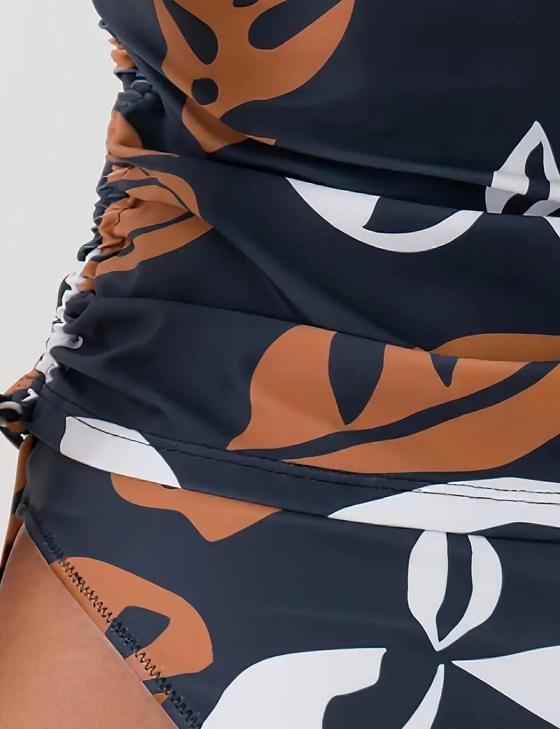 Costume da bagno intero donna con stampa foglie tropicali marroni e bianche su sfondo nero, design arricciato, moda mare estate.