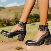 Scarpe nere con tacco largo e cinturini, indossate all'aperto su sfondo naturale. Eleganti e versatili, ideali per moda e comfort.