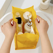 Mani che organizzano prodotti per la cura personale in una borsa gialla. Contenitori con dispenser e flaconi, accessori bagno, ordine e pulizia.