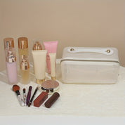Set di cosmetici su tavolo bianco: flaconi crema, rossetto, pennelli trucco, specchio e pochette trasparente. Prodotti bellezza e cura pelle.