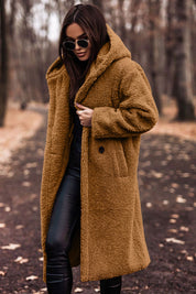 Donna con cappotto teddy marrone, occhiali da sole neri, pantaloni in pelle nera, passeggia in un parco autunnale. Moda invernale, stile casual chic.