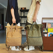 Due persone con zaini CLIOO beige e verde in un ambiente interno moderno. Zaini leggeri, tasche frontali, stile casual.
