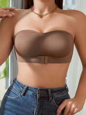 Donna con reggiseno senza spalline marrone, chiusura frontale, indossa jeans a vita alta. Moda intima femminile, comfort e stile.