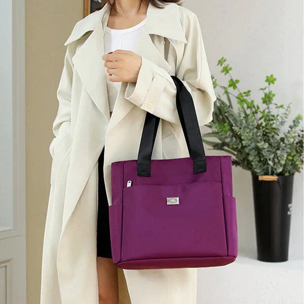 Donna con cappotto bianco indossa borsa a tracolla viola, elegante e spaziosa, perfetta per l'uso quotidiano. Accessorio moda femminile.