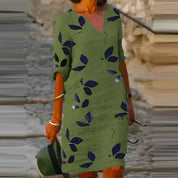 Abito verde con motivo a foglie blu, maniche a tre quarti, scollo a V, indossato da donna all'aperto. Moda estiva casual elegante.