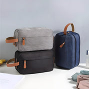 Tre eleganti borse da toilette in tessuto grigio, nero e blu con manici in pelle, ideali per viaggi e organizzazione. Design moderno e funzionale.