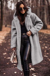 Donna con cappotto in pelliccia sintetica grigia, occhiali da sole, pantaloni in pelle nera, borsa beige, in un parco autunnale. Moda autunno inverno.