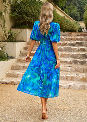 Donna con abito lungo floreale blu e verde, maniche a sbuffo, su scala di pietra. Moda estiva elegante, abbigliamento femminile casual chic.