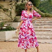 Donna con abito floreale rosa e bianco, occhiali da sole, borsa intrecciata, su gradini di pietra. Moda estiva elegante, abbigliamento femminile trendy.