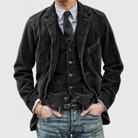 Giacca uomo in velluto nero, abbinata a gilet e cravatta, su camicia a righe. Look casual con jeans. Moda maschile elegante e moderna.