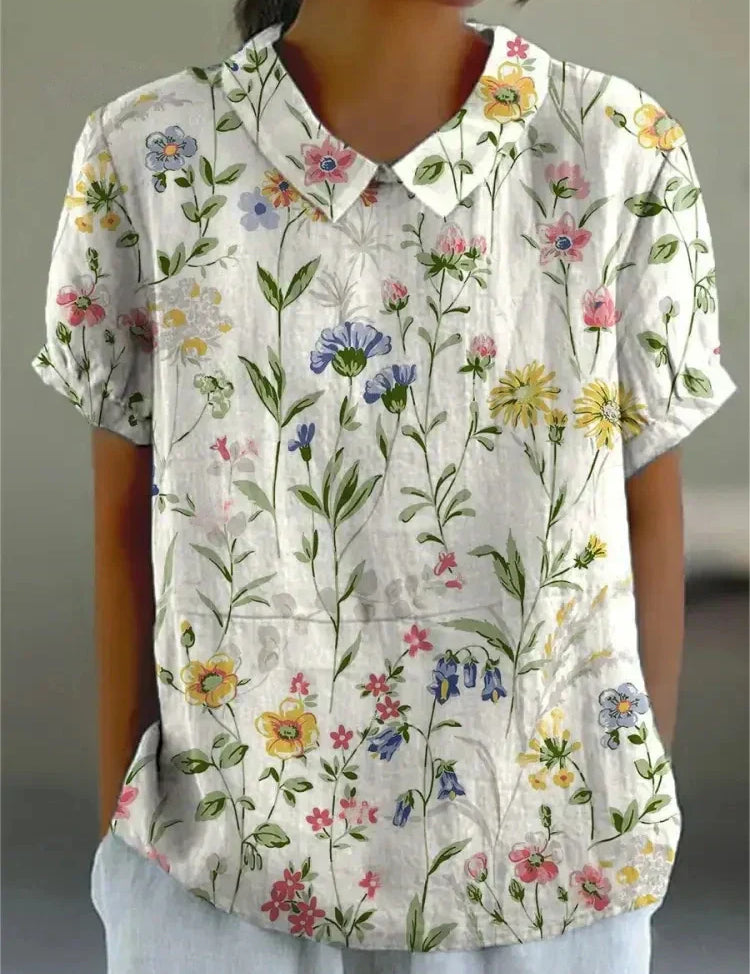 Camicia donna a maniche corte con stampa floreale colorata su sfondo bianco, colletto classico. Moda estiva casual, tessuto leggero.