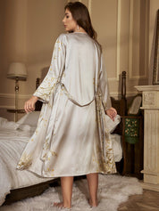 Donna in camera da letto indossa vestaglia di seta grigia con motivi floreali dorati, elegante e lussuosa, perfetta per comfort e stile notturno.