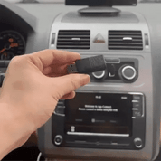 Mano che tiene un adattatore Bluetooth USB per auto davanti al cruscotto. Tecnologia wireless per connettività audio e chiamate in vivavoce.