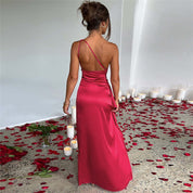 Abito lungo rosso elegante in raso, spallina sottile, schiena scoperta, circondato da petali di rosa e candele bianche su pavimento grigio.