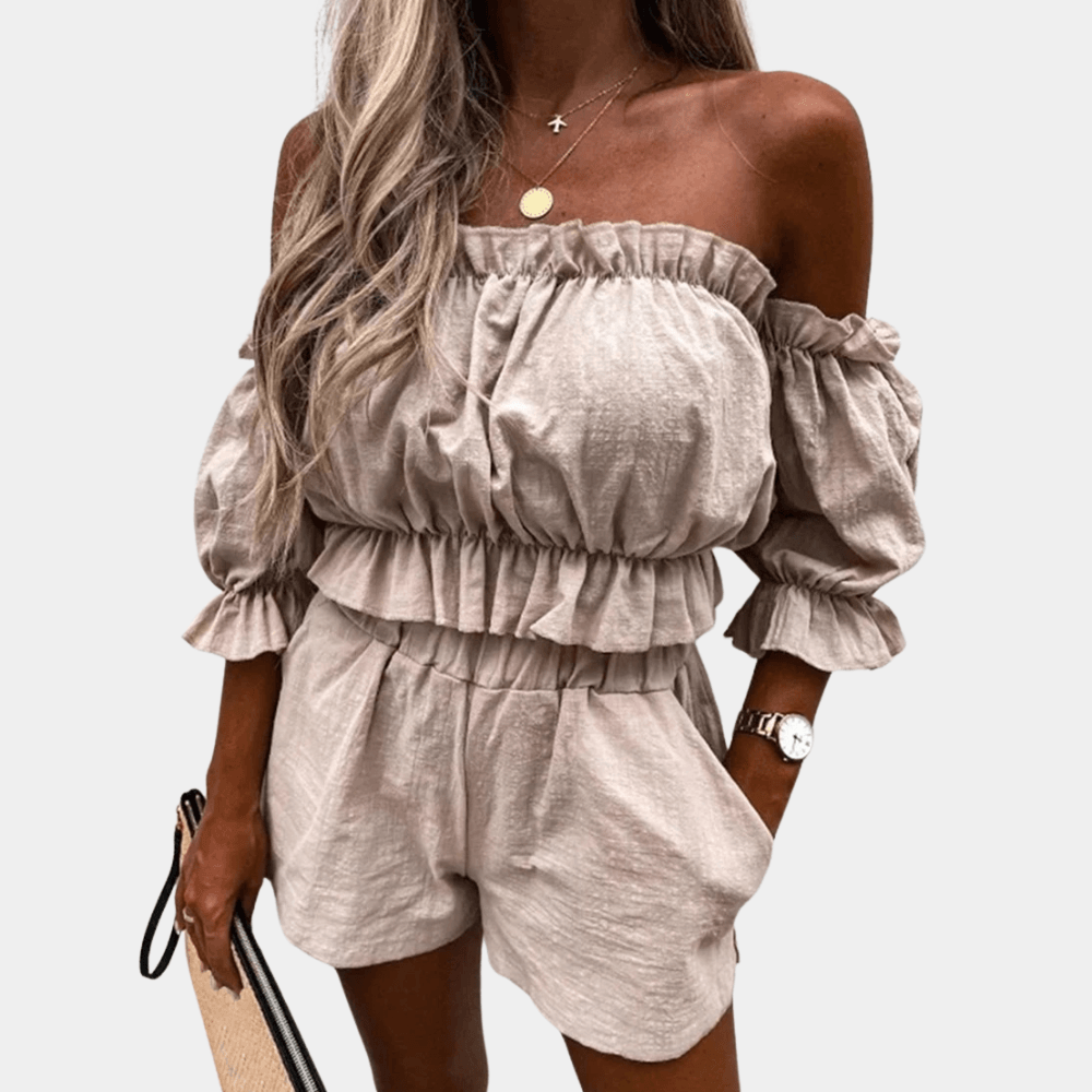 Donna con completo estivo beige, top a spalle scoperte e pantaloncini, accessoriata con borsa e orologio. Moda femminile casual elegante.