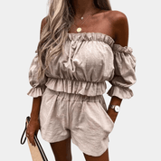 Donna con completo estivo beige, top a spalle scoperte e pantaloncini, accessoriata con borsa e orologio. Moda femminile casual elegante.