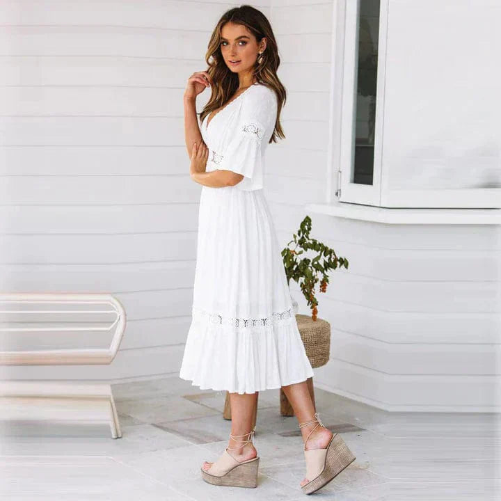 Donna in abito bianco estivo con dettagli in pizzo, sandali con zeppa beige, posa elegante su sfondo bianco. Moda femminile, abbigliamento estivo.