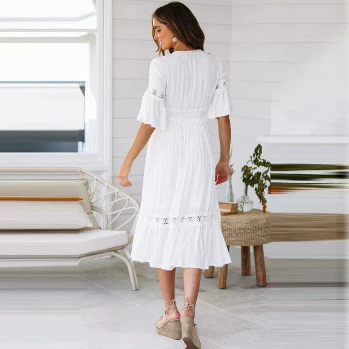 Donna in abito bianco estivo, maniche corte, lunghezza media, in piedi in una stanza luminosa. Elegante e casual, perfetto per giornate calde.