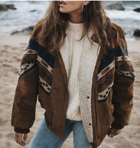 Giacca invernale donna in lana e pelle scamosciata con motivo etnico, indossata su spiaggia. Maglione bianco, jeans, stile casual autunnale.