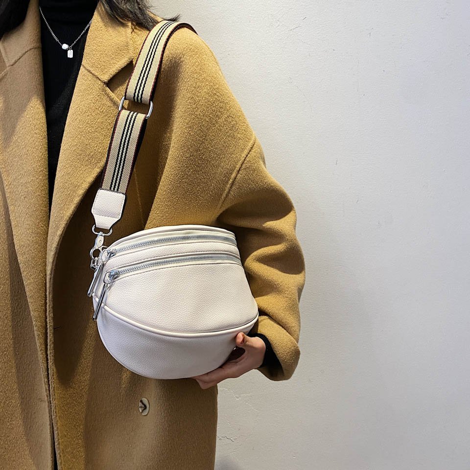 Cappotto beige donna con borsa a tracolla bianca, design moderno, cerniere multiple, moda autunno inverno, accessorio elegante e pratico.