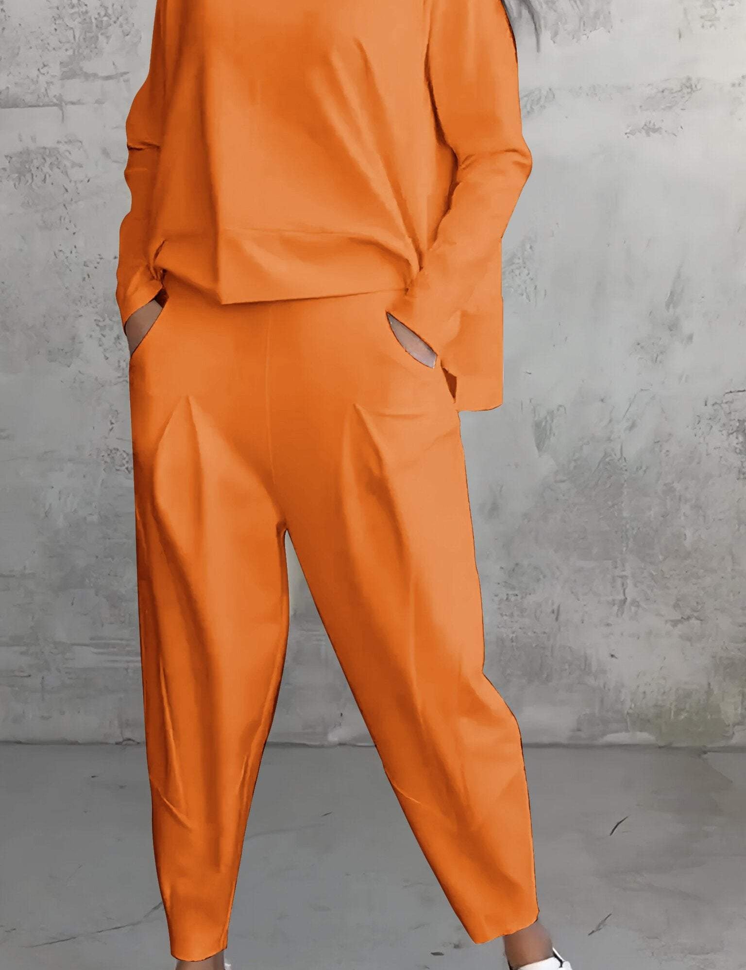 Donna in tuta arancione oversize, con pantaloni larghi e maglia a maniche lunghe, indossa sneakers bianche. Moda casual, abbigliamento autunnale.