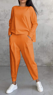 Donna in tuta arancione oversize, con pantaloni larghi e maglia a maniche lunghe, indossa sneakers bianche. Moda casual, abbigliamento autunnale.