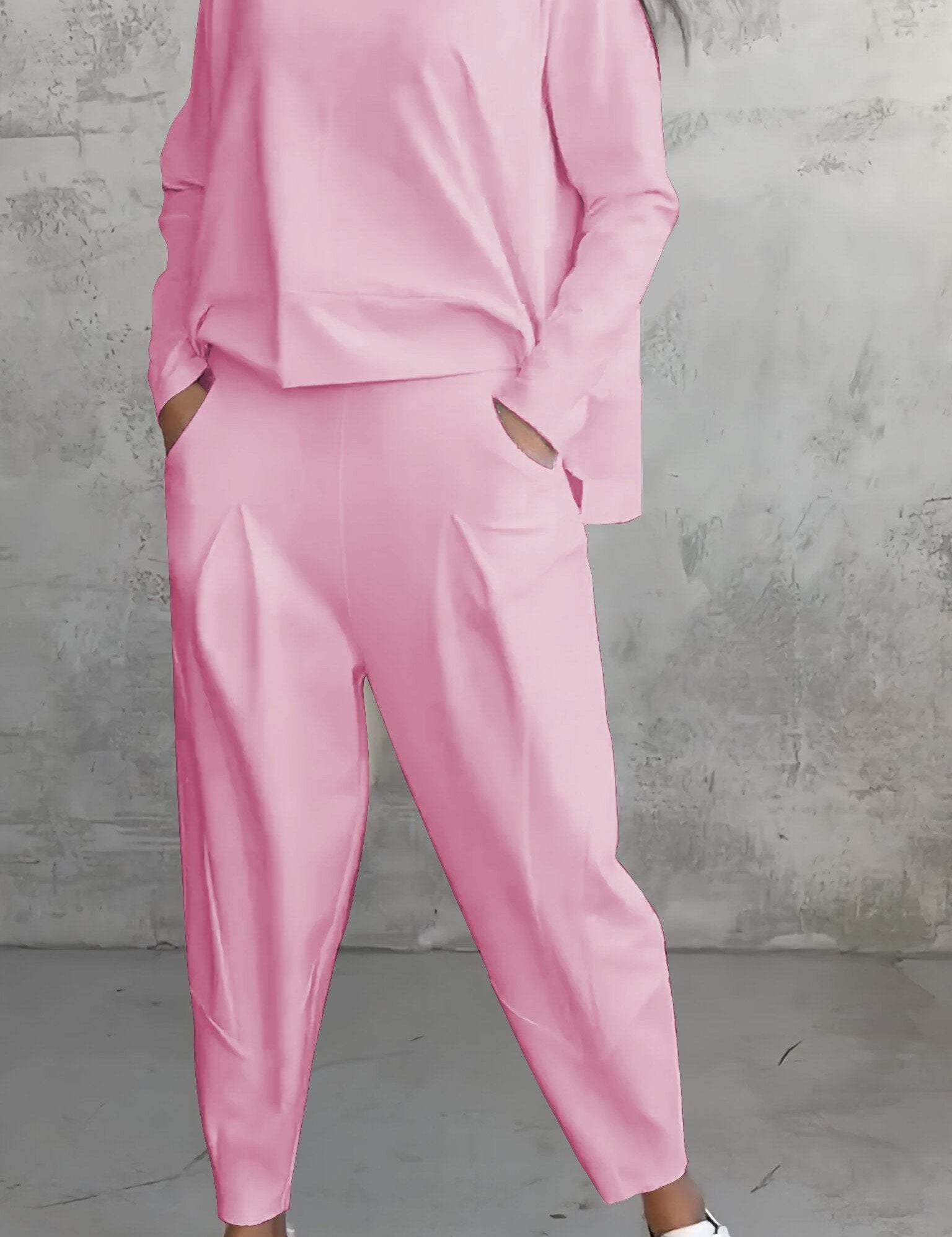 Completo donna rosa pastello, maglia e pantaloni larghi, tasche laterali, abbinato a sneakers bianche, sfondo grigio minimalista.