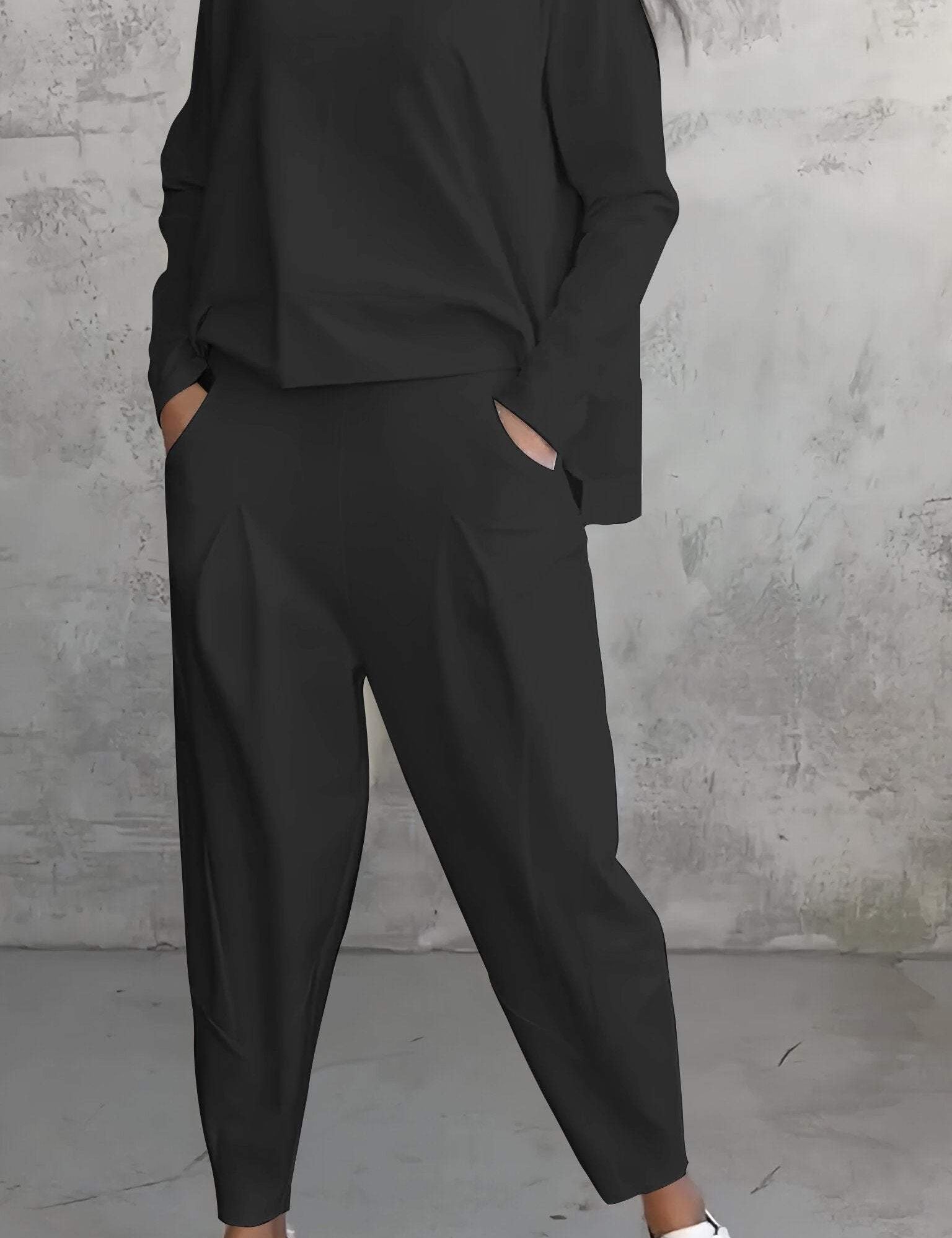 Donna in tuta nera casual con pantaloni larghi e maglia a maniche lunghe, indossa sneakers bianche. Look moderno e comodo per il tempo libero.