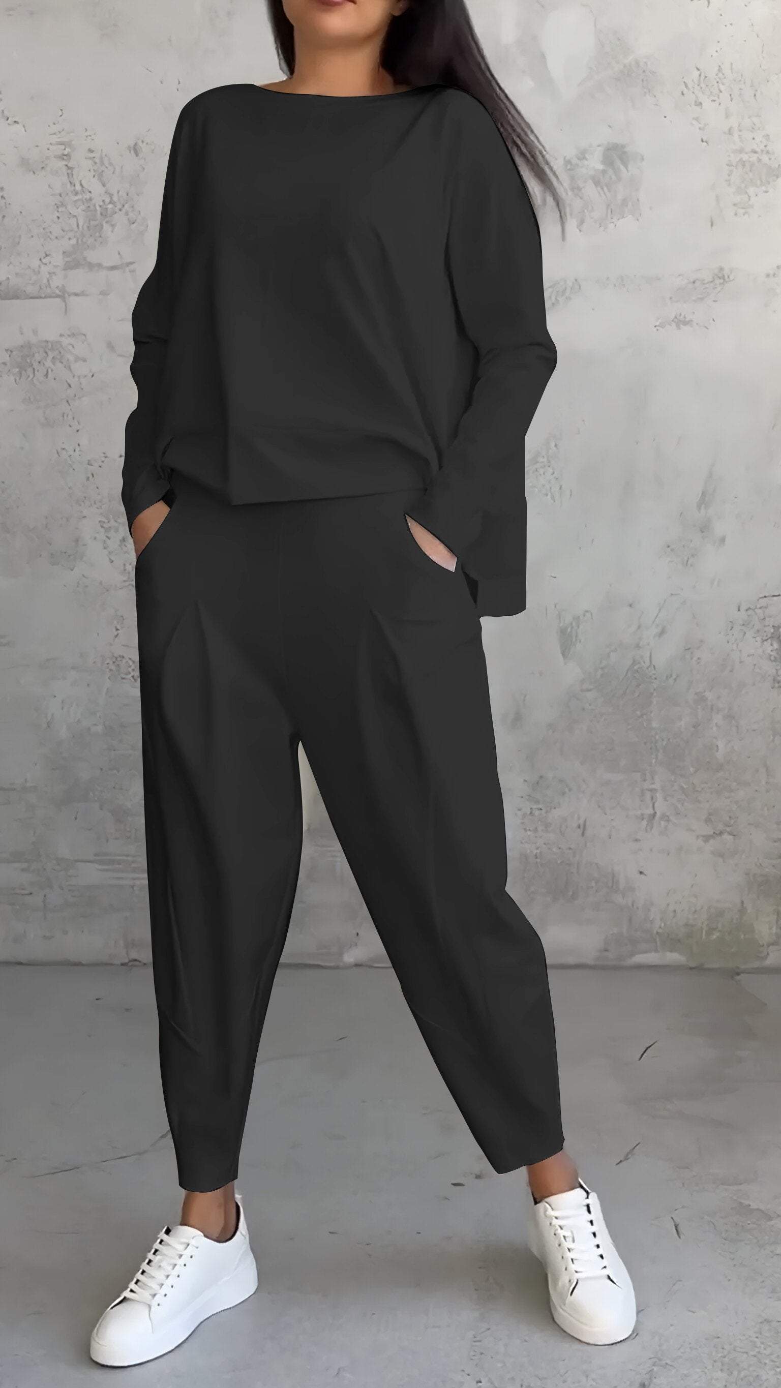 Donna in tuta nera casual con pantaloni larghi e maglia a maniche lunghe, indossa sneakers bianche. Look moderno e comodo per il tempo libero.