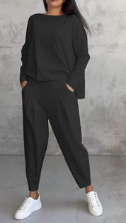 Donna in tuta nera casual con pantaloni larghi e maglia a maniche lunghe, indossa sneakers bianche. Look moderno e comodo per il tempo libero.