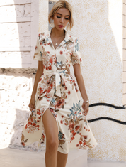 Donna con abito floreale estivo, maniche corte, cintura in vita, sfondo urbano. Moda femminile elegante, abbigliamento casual chic.