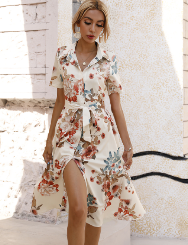 Donna con abito floreale estivo, maniche corte, cintura in vita, sfondo urbano. Moda femminile elegante, abbigliamento casual chic.