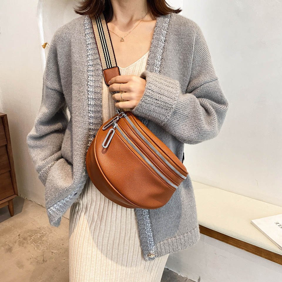 Donna con cardigan grigio e borsa a tracolla in pelle marrone, abito a righe beige. Moda autunnale, accessori eleganti, stile casual chic.