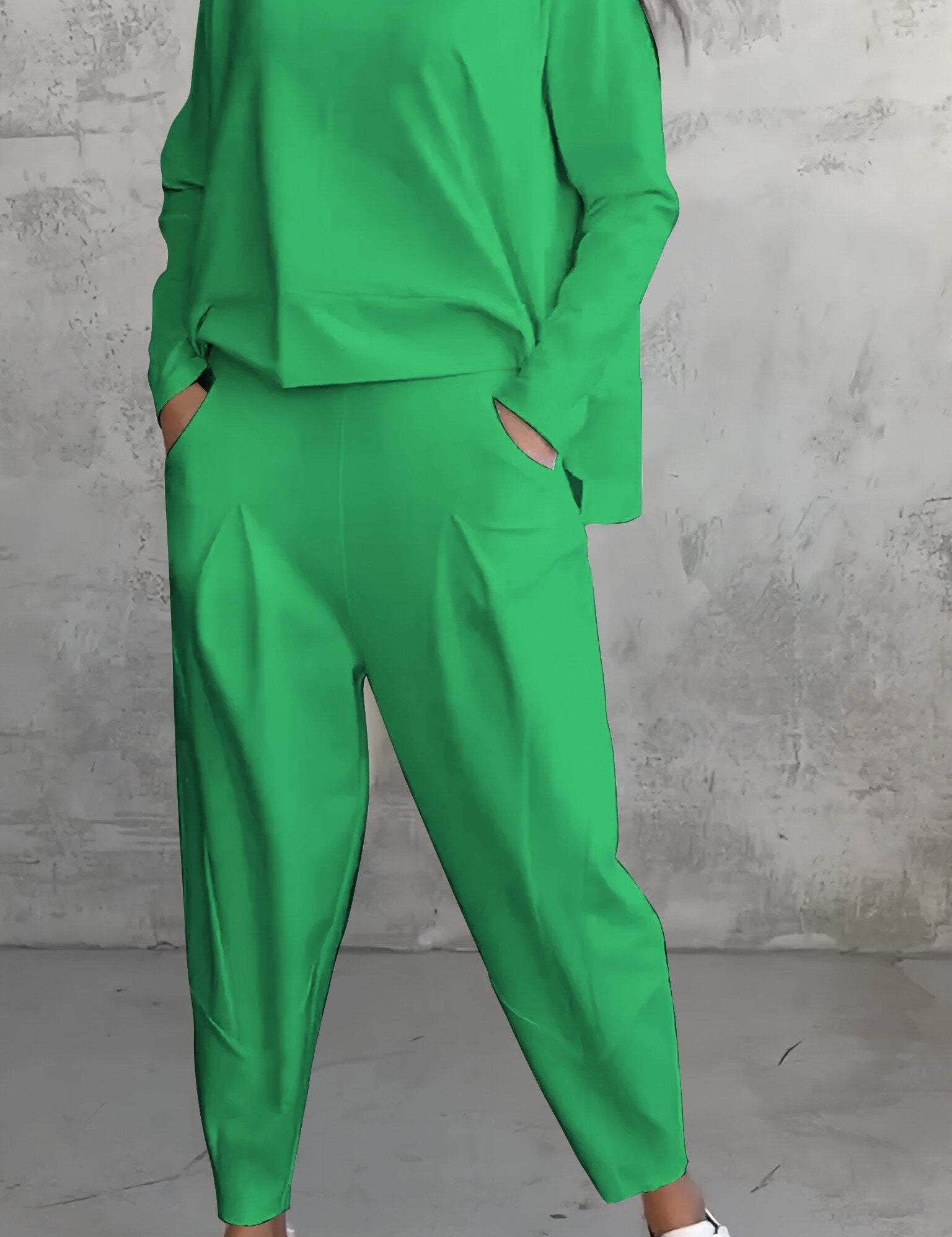Donna in tuta verde brillante con pantaloni larghi e maglia a maniche lunghe, indossa sneakers bianche. Sfondo grigio minimalista.