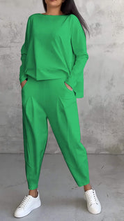 Donna in tuta verde brillante con pantaloni larghi e maglia a maniche lunghe, indossa sneakers bianche. Sfondo grigio minimalista.
