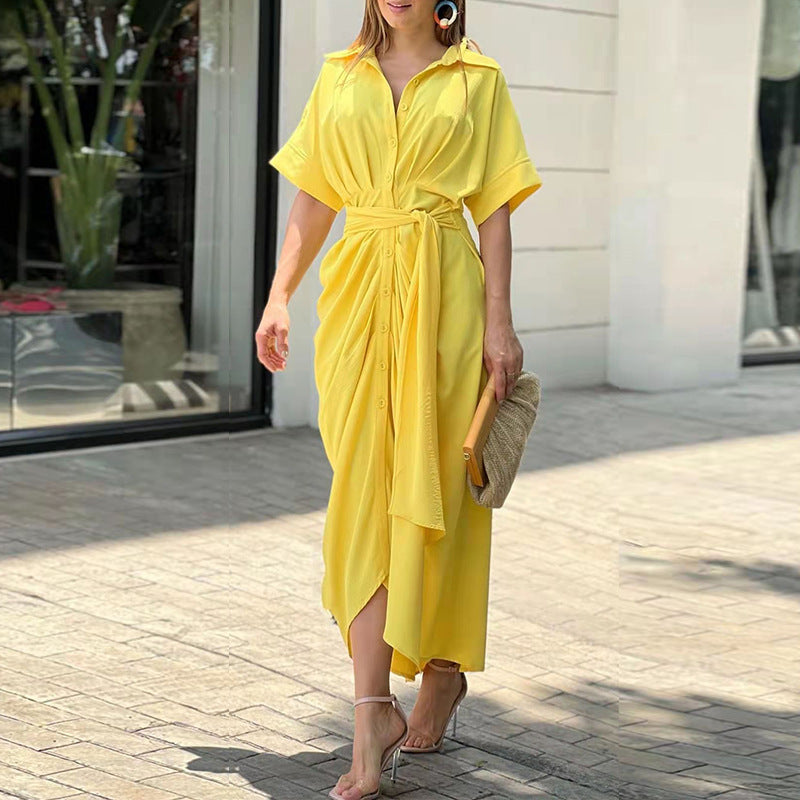 Donna con abito lungo giallo, cintura in vita, sandali eleganti e borsa a mano beige. Moda estiva, abbigliamento casual chic, passeggiata urbana.
