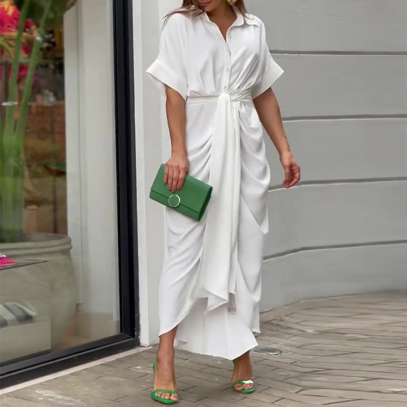 Donna con abito bianco elegante e borsa verde, sandali coordinati, posa vicino a una vetrina. Moda estiva, stile chic, abbigliamento femminile.