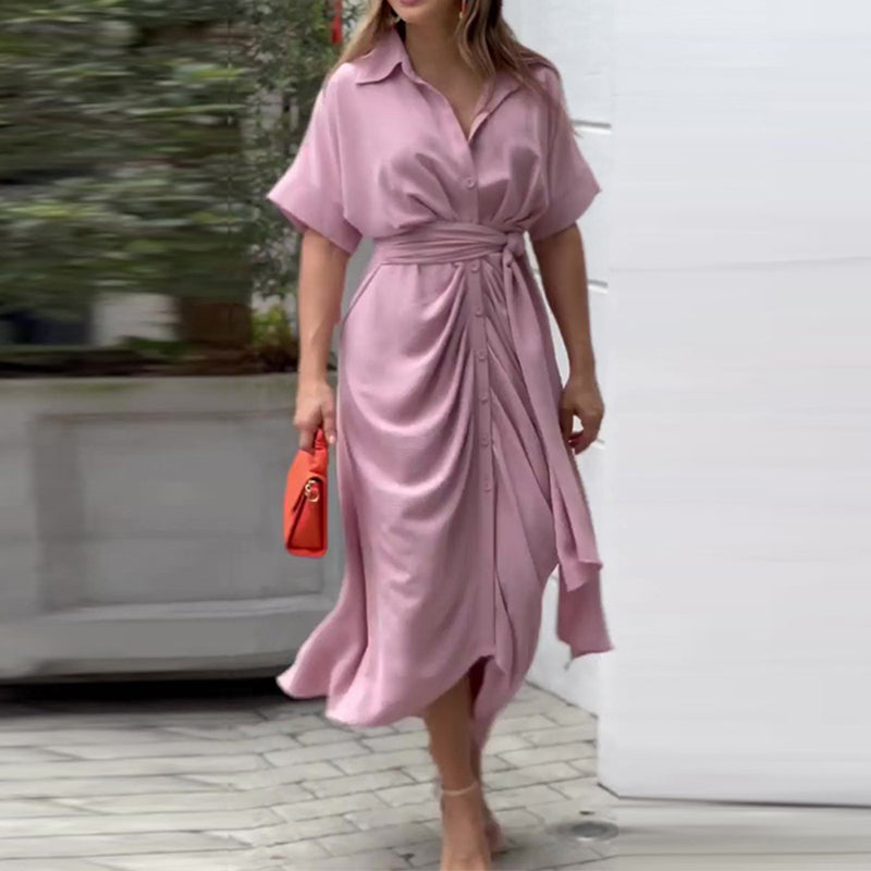 Donna con abito lungo rosa, cintura in vita, maniche corte, cammina con borsa arancione. Moda estiva elegante, abbigliamento femminile casual.