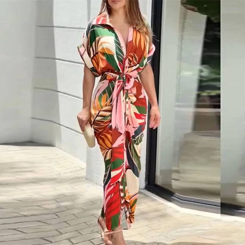 Abito lungo estivo a fantasia tropicale multicolore, maniche corte, nodo frontale, indossato da donna. Moda femminile, abbigliamento estivo elegante.