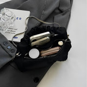 Borsa a tracolla nera in raso con catena argento, contenente smartphone, portafoglio e accessori, su giacca grigia. Elegante e pratica.