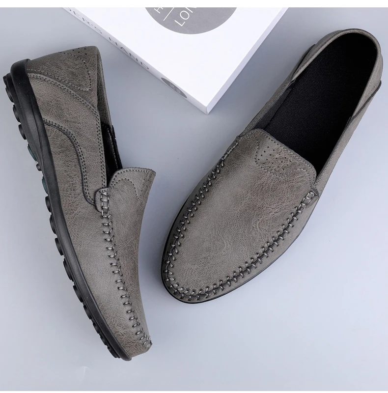 Mocassini uomo in pelle grigia, suola antiscivolo nera, design elegante e casual, ideali per abbigliamento quotidiano e occasioni formali.