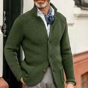 Giacca cardigan uomo verde oliva, maglia a coste, abbinata a camicia bianca e foulard blu. Moda maschile elegante e casual.