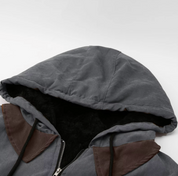Giacca invernale con cappuccio grigio, dettagli in pelle marrone, chiusura a zip, interno foderato in pelliccia sintetica. Abbigliamento caldo e alla moda.