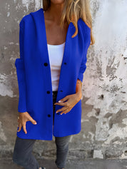 Donna indossa cardigan blu acceso su top bianco e jeans grigi, sfondo muro grigio. Moda casual autunnale, abbigliamento femminile trendy.