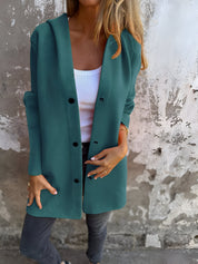 Donna con cappotto verde acqua, maglia bianca e jeans grigi davanti a muro rustico. Moda autunnale, abbigliamento casual elegante.