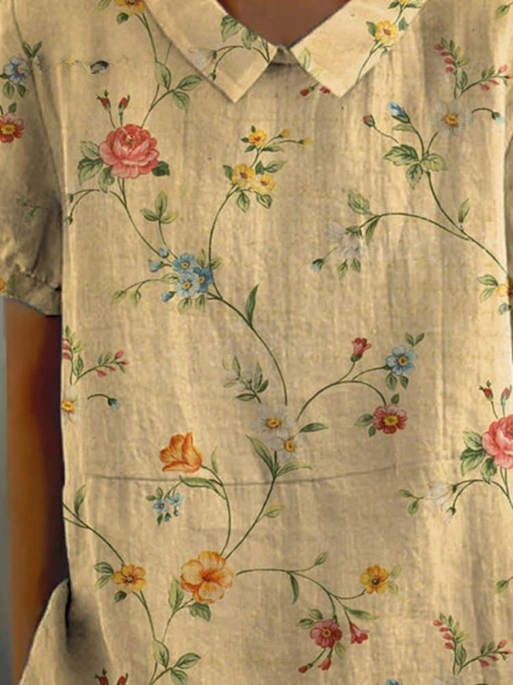 Camicia beige con colletto, decorata con fiori colorati e foglie verdi. Design floreale elegante, ideale per moda estiva e abbigliamento casual.